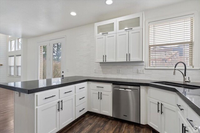 kitchen with stainless steel dishwasher, backsplash, a sink, and a peninsula