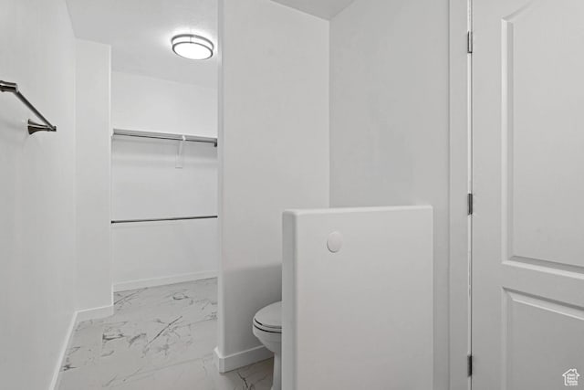 full bathroom featuring baseboards, marble finish floor, toilet, and a spacious closet