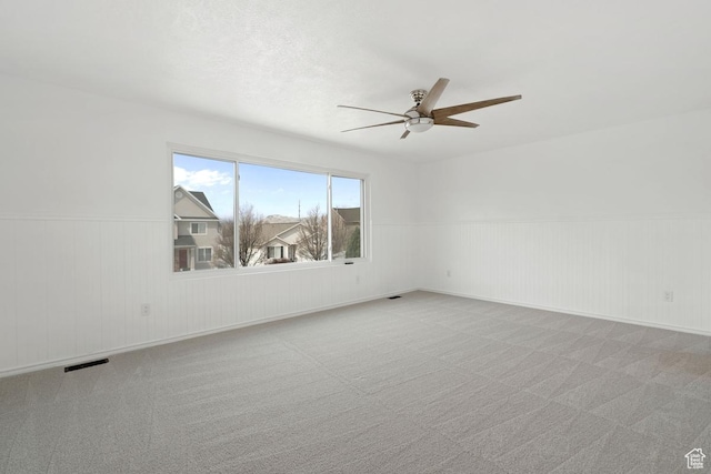 unfurnished room with carpet, visible vents, a ceiling fan, and wainscoting