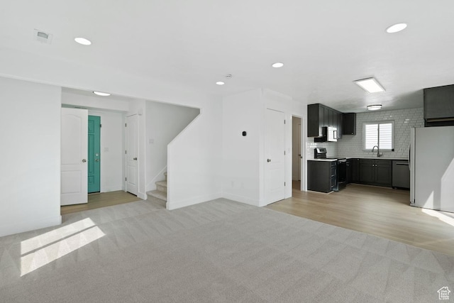 unfurnished living room with stairway, a sink, light colored carpet, visible vents, and recessed lighting