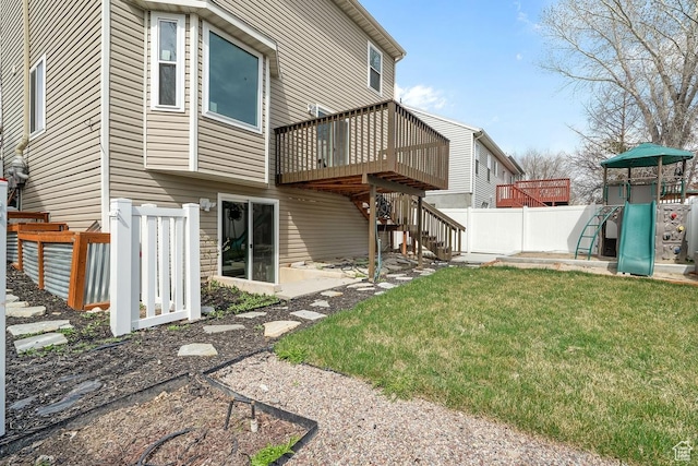 rear view of house with fence, a wooden deck, a playground, stairway, and a yard