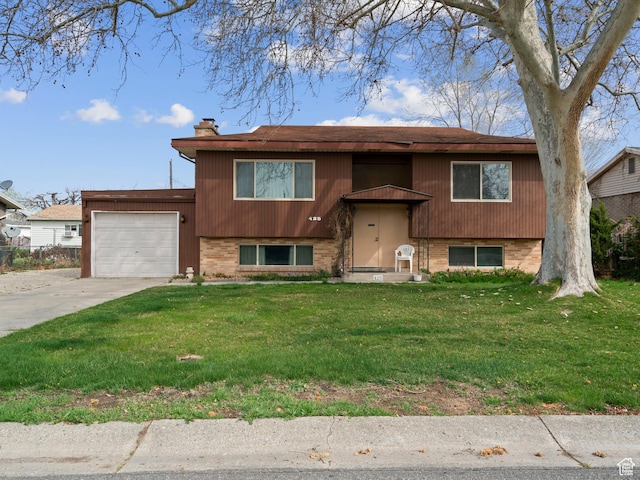 raised ranch with concrete driveway, an attached garage, a front yard, brick siding, and a chimney