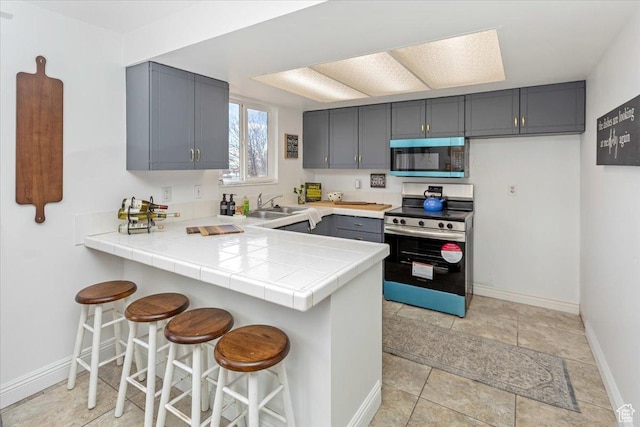 kitchen with a peninsula, appliances with stainless steel finishes, a sink, gray cabinetry, and a breakfast bar area