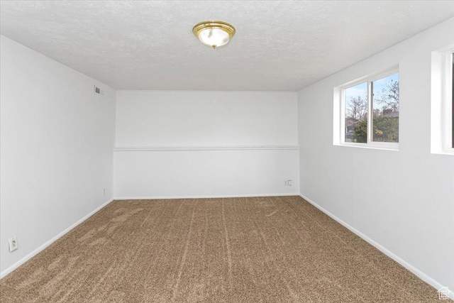 spare room with carpet floors, baseboards, visible vents, and a textured ceiling