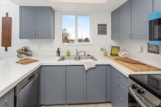 kitchen featuring tile counters, gray cabinets, a sink, and stainless steel appliances