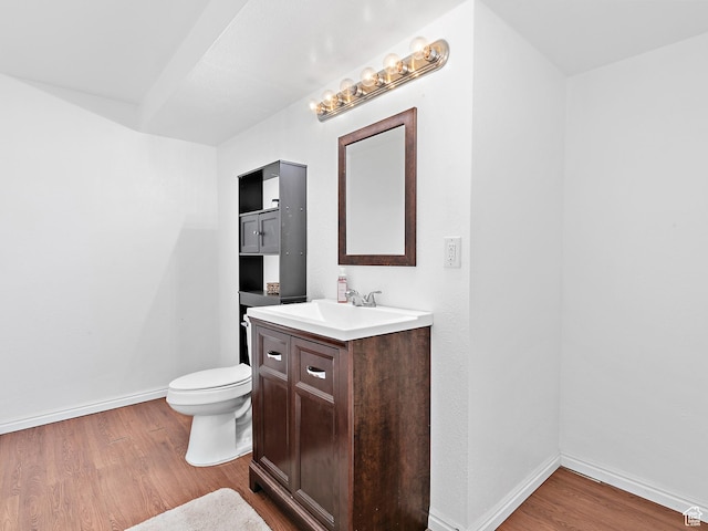 half bathroom featuring toilet, vanity, baseboards, and wood finished floors