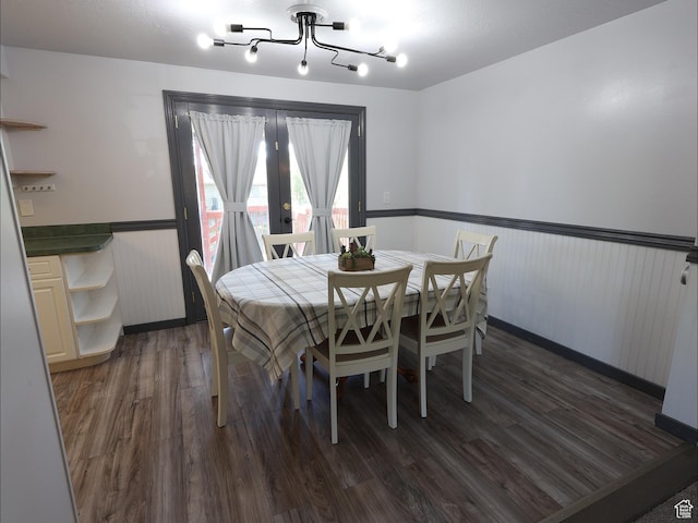 dining room with dark wood finished floors, a wainscoted wall, french doors, and a chandelier