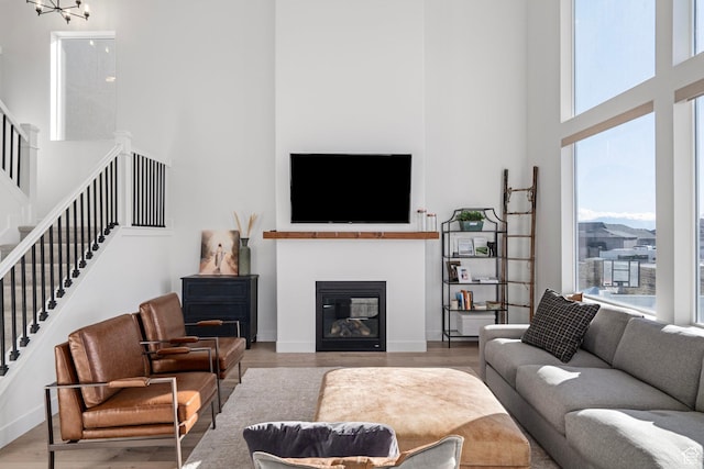living room featuring stairway, baseboards, a towering ceiling, a glass covered fireplace, and wood finished floors
