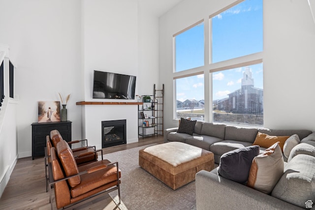 living area featuring baseboards, a towering ceiling, wood finished floors, and a glass covered fireplace