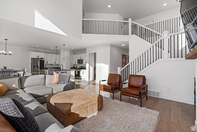 living room featuring stairs, an inviting chandelier, a towering ceiling, visible vents, and light wood-style flooring