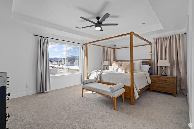 bedroom featuring baseboards, a raised ceiling, ceiling fan, visible vents, and light carpet