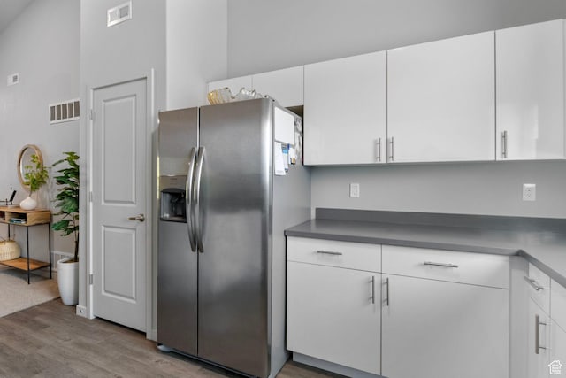 kitchen with stainless steel fridge with ice dispenser, white cabinets, visible vents, and wood finished floors