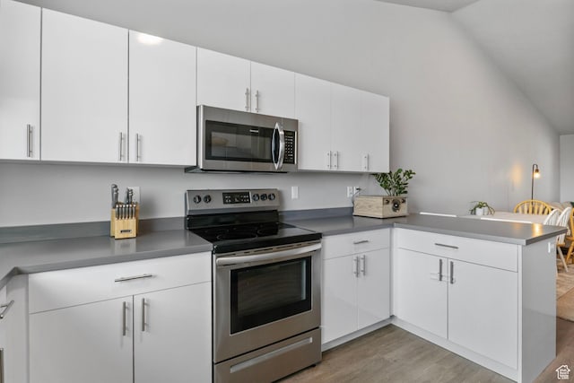 kitchen with white cabinets, light wood-style flooring, a peninsula, stainless steel appliances, and vaulted ceiling