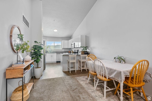 dining room featuring high vaulted ceiling, a textured ceiling, and visible vents