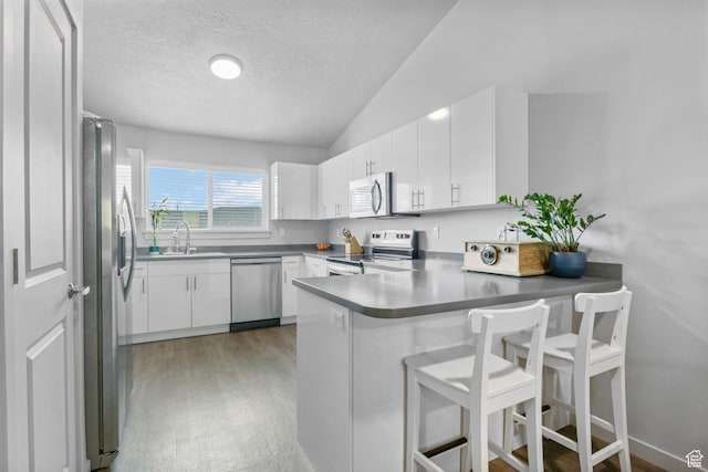 kitchen featuring white cabinets, light wood-style flooring, a peninsula, stainless steel appliances, and lofted ceiling