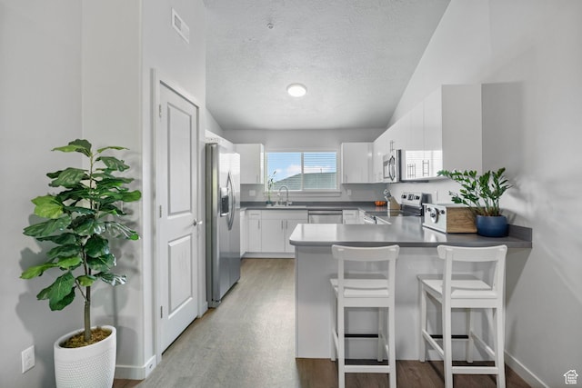 kitchen with visible vents, a peninsula, appliances with stainless steel finishes, a sink, and light wood-style floors