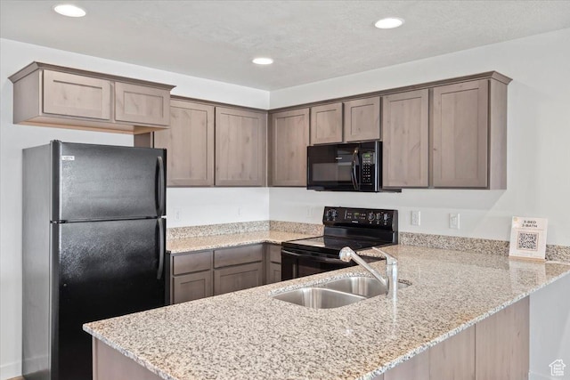kitchen featuring light stone countertops, a peninsula, black appliances, recessed lighting, and a sink