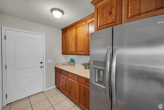 2367 N Monarch Cir E, Cedar City, UT 84721 - kitchen with stainless steel fridge, light countertops, backsplash, light tile patterned floors, and brown cabinetry