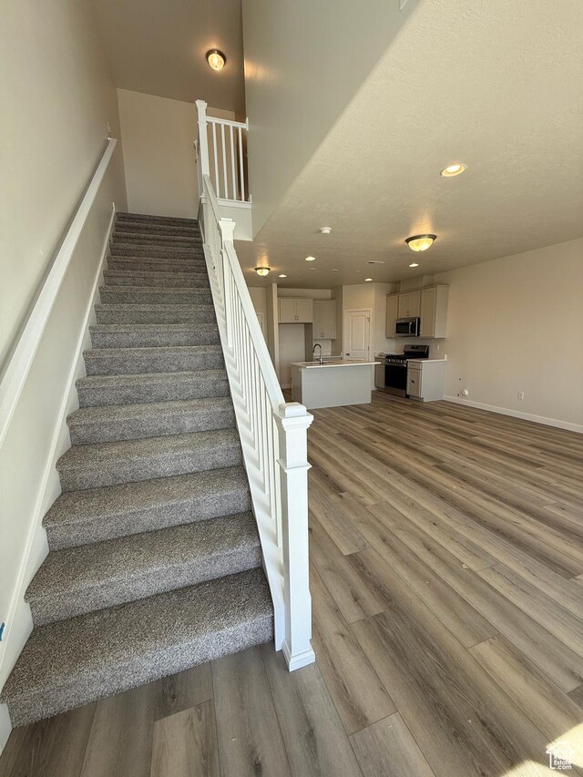 stairway with baseboards, wood finished floors, and recessed lighting