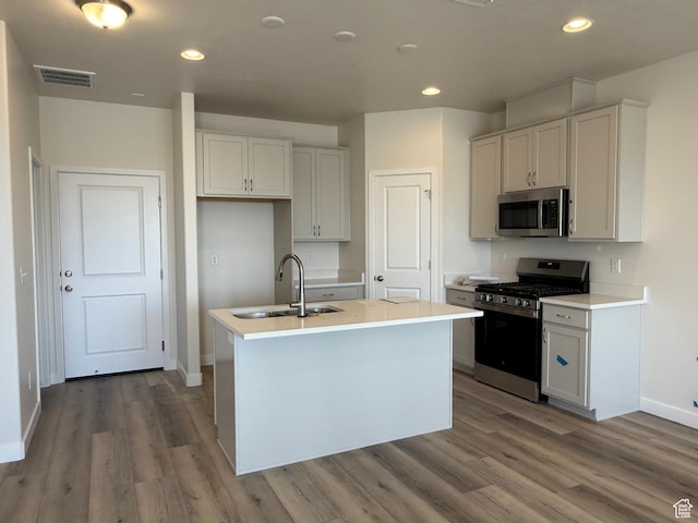 kitchen featuring visible vents, wood finished floors, appliances with stainless steel finishes, a sink, and an island with sink