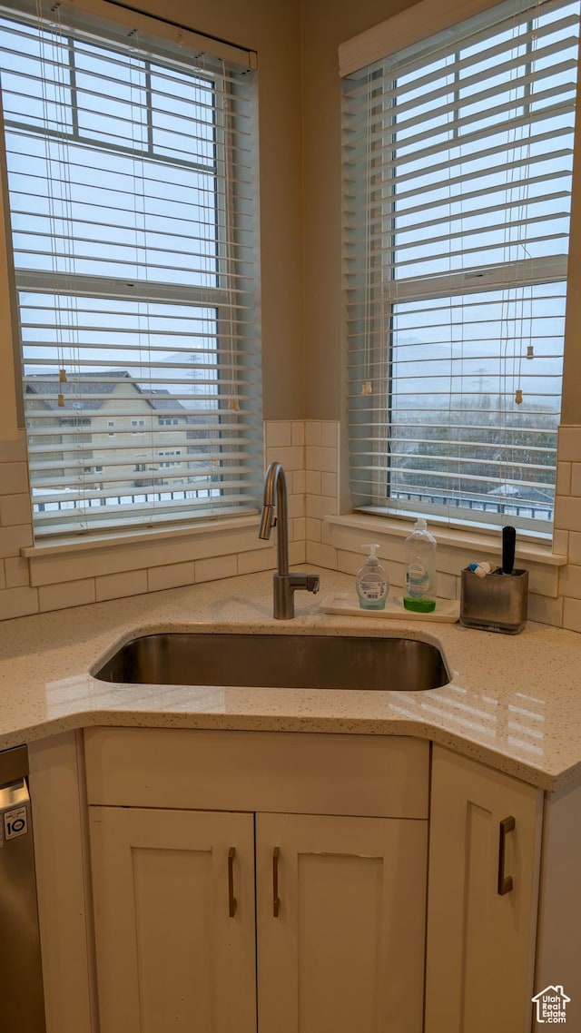 kitchen with a sink, white cabinetry, tasteful backsplash, light stone countertops, and stainless steel dishwasher