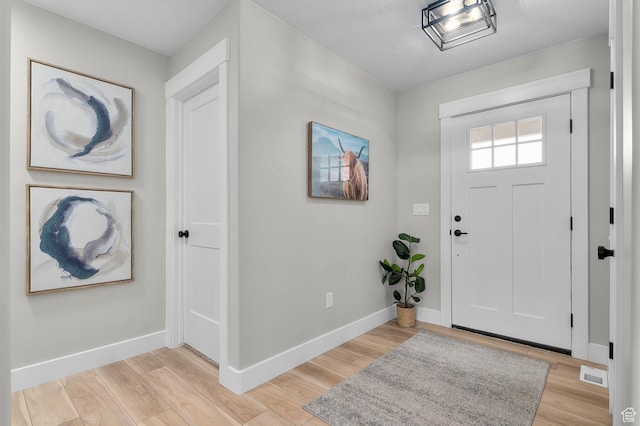 foyer entrance with light wood-style floors, baseboards, and visible vents