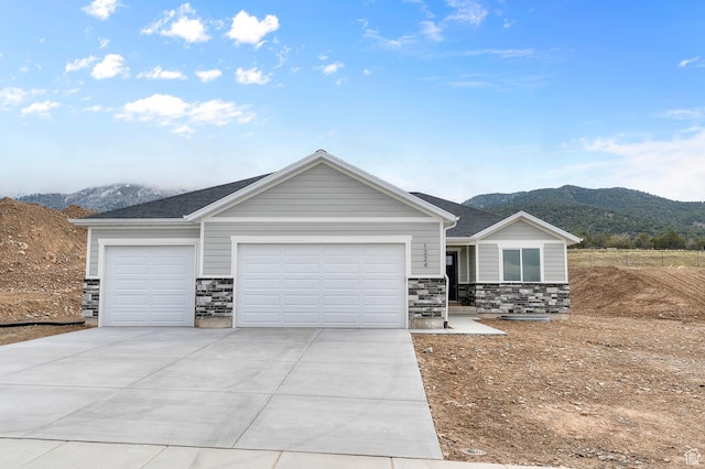 view of front of property with an attached garage, driveway, stone siding, and a mountain view