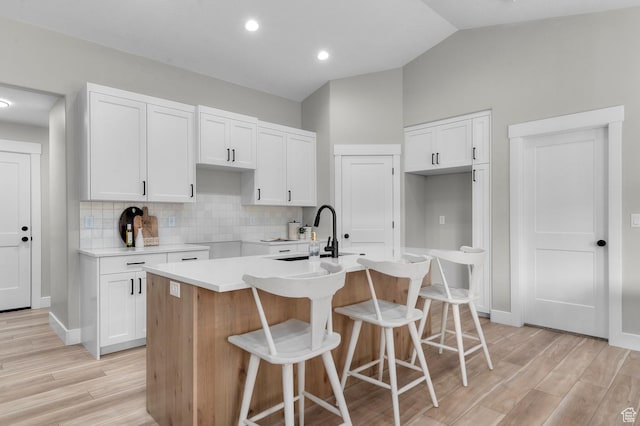kitchen featuring light wood-style flooring, a kitchen island with sink, a sink, and white cabinets