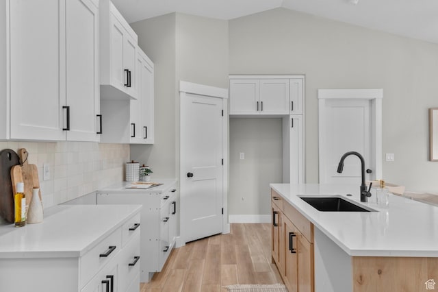 kitchen featuring tasteful backsplash, vaulted ceiling, light countertops, a sink, and light wood finished floors
