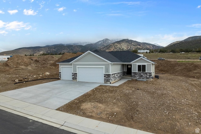 single story home featuring an attached garage, driveway, a mountain view, and stone siding