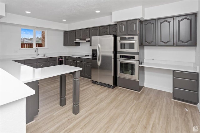 kitchen with light wood-type flooring, stainless steel appliances, under cabinet range hood, a textured ceiling, and a sink