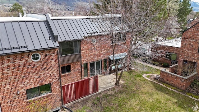 view of property exterior with a lawn, brick siding, a standing seam roof, and metal roof