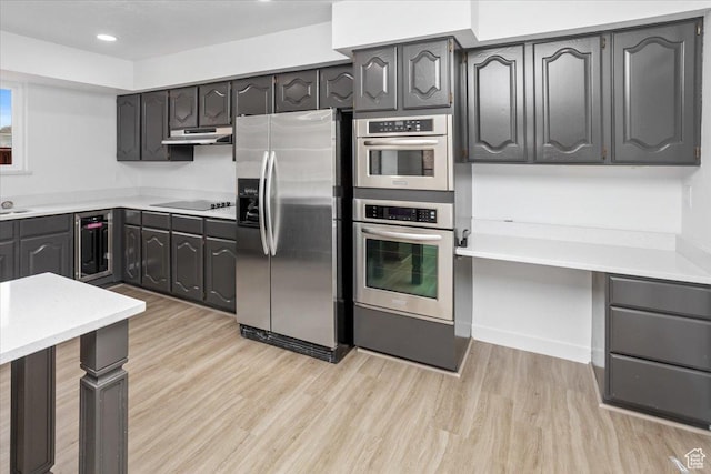 kitchen featuring light countertops, light wood finished floors, beverage cooler, under cabinet range hood, and stainless steel appliances