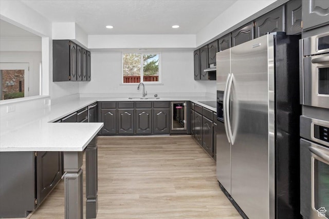 kitchen featuring light countertops, a sink, beverage cooler, light wood-type flooring, and stainless steel appliances