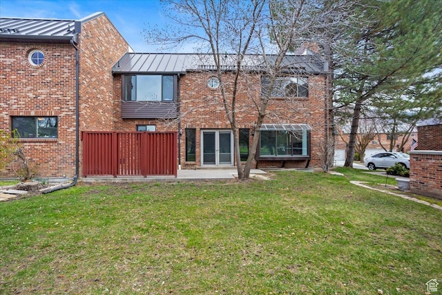 back of property featuring a standing seam roof, metal roof, french doors, brick siding, and a lawn
