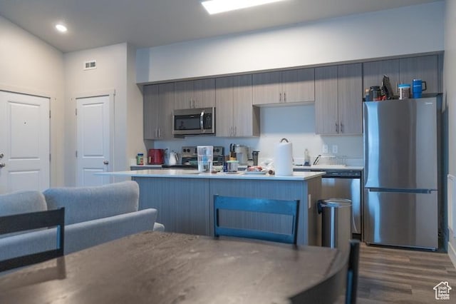 kitchen with light countertops, stainless steel appliances, a kitchen island, dark wood-style floors, and visible vents