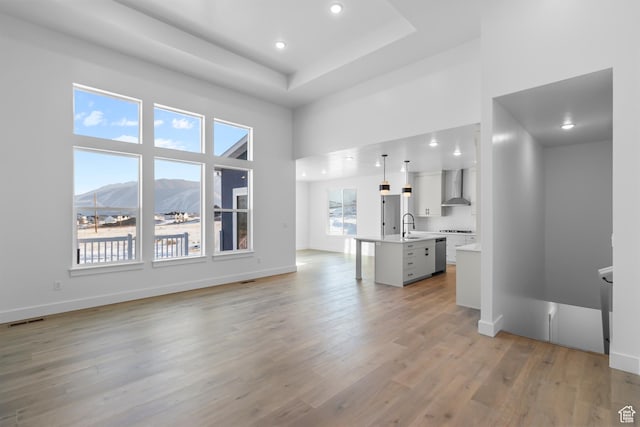 unfurnished living room featuring baseboards, a sink, a towering ceiling, visible vents, and light wood-style flooring