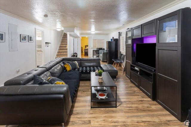 living room featuring a textured ceiling, electric panel, crown molding, stairway, and light wood-type flooring