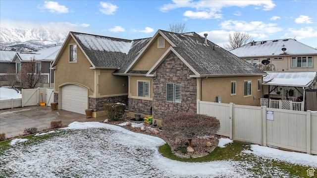 view of front facade featuring stone siding, a gate, fence, a garage, and stucco siding