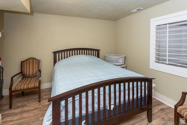 bedroom featuring baseboards, visible vents, wood finished floors, and a textured ceiling