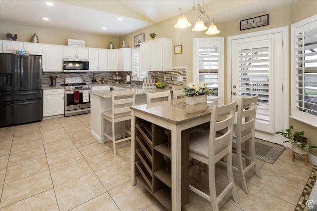 kitchen featuring light tile patterned flooring, backsplash, light stone countertops, appliances with stainless steel finishes, and white cabinets