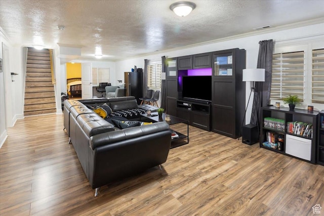 living area featuring a textured ceiling, visible vents, crown molding, stairs, and light wood-style floors
