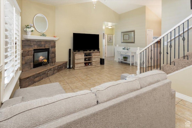 living area with baseboards, tile patterned floors, stairway, a stone fireplace, and vaulted ceiling