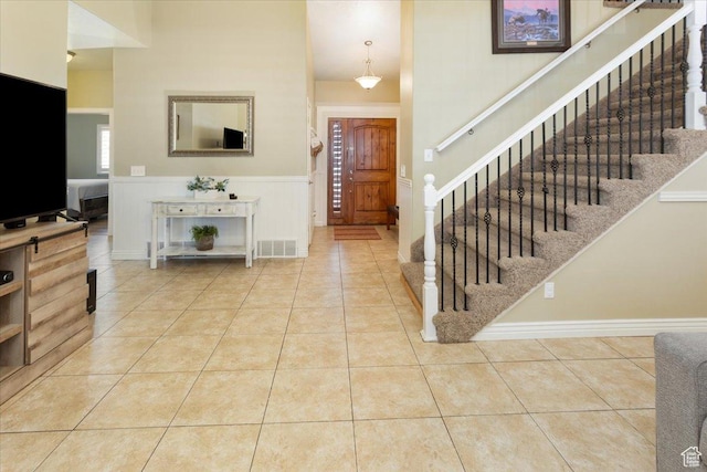 tiled foyer entrance with stairs, wainscoting, a high ceiling, and visible vents