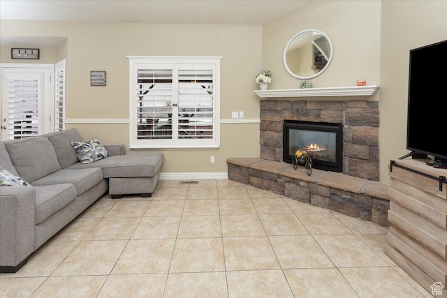 living room with a stone fireplace, baseboards, visible vents, and tile patterned flooring