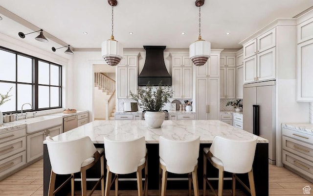 kitchen with light wood finished floors, dishwasher, a kitchen island, a sink, and custom range hood