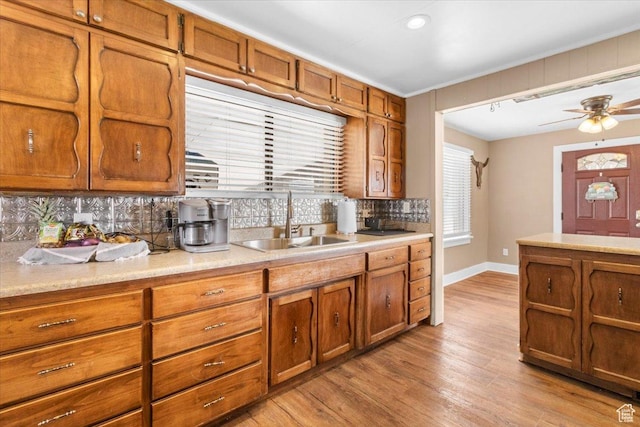 kitchen featuring light countertops, backsplash, a sink, light wood finished floors, and brown cabinetry