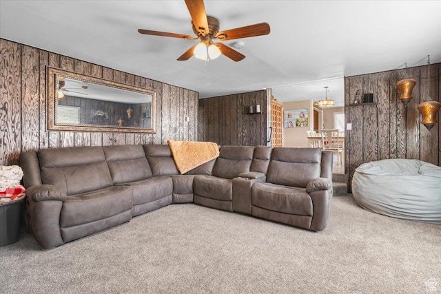 living room featuring ceiling fan with notable chandelier, wood walls, and carpet floors