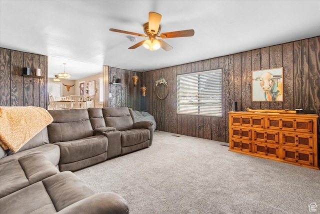carpeted living room featuring wood walls and ceiling fan with notable chandelier