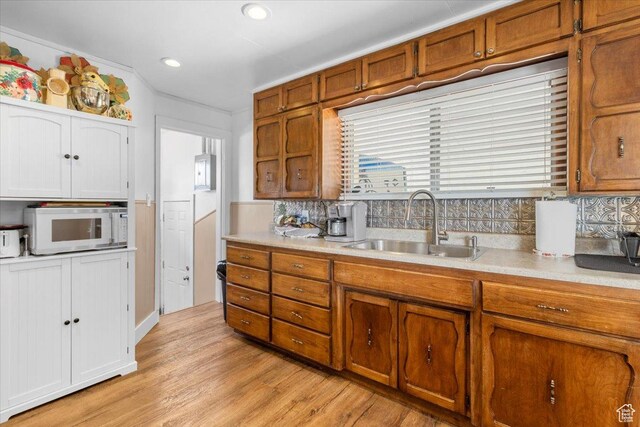 kitchen with white microwave, a sink, brown cabinetry, and light countertops